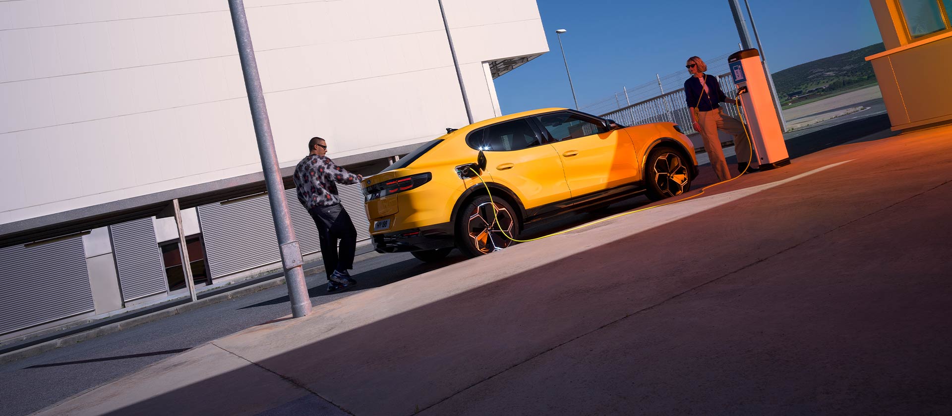 Lidé nabíjející žlutý Ford Capri EV u veřejné nabíjecí stanice.
