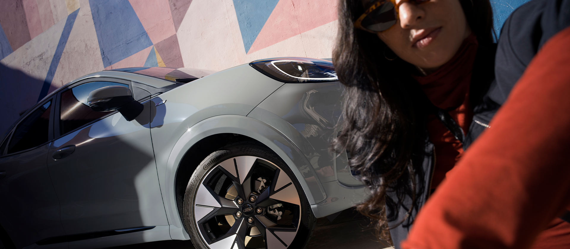 Osoba sedící vedle stříbrného mild-hybridního vozu Ford Puma.