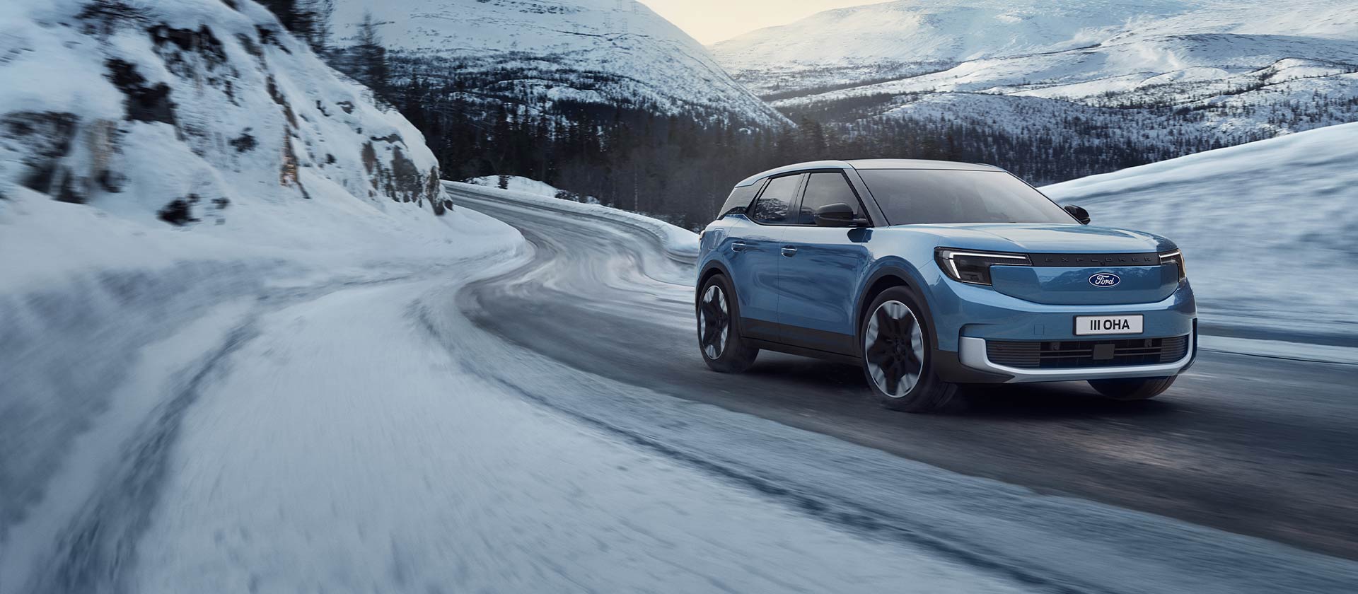 Modrý elektromobil Ford Explorer na zasněžené horské silnici, který zdůrazňuje své schopnosti a dojezd v zimních podmínkách.