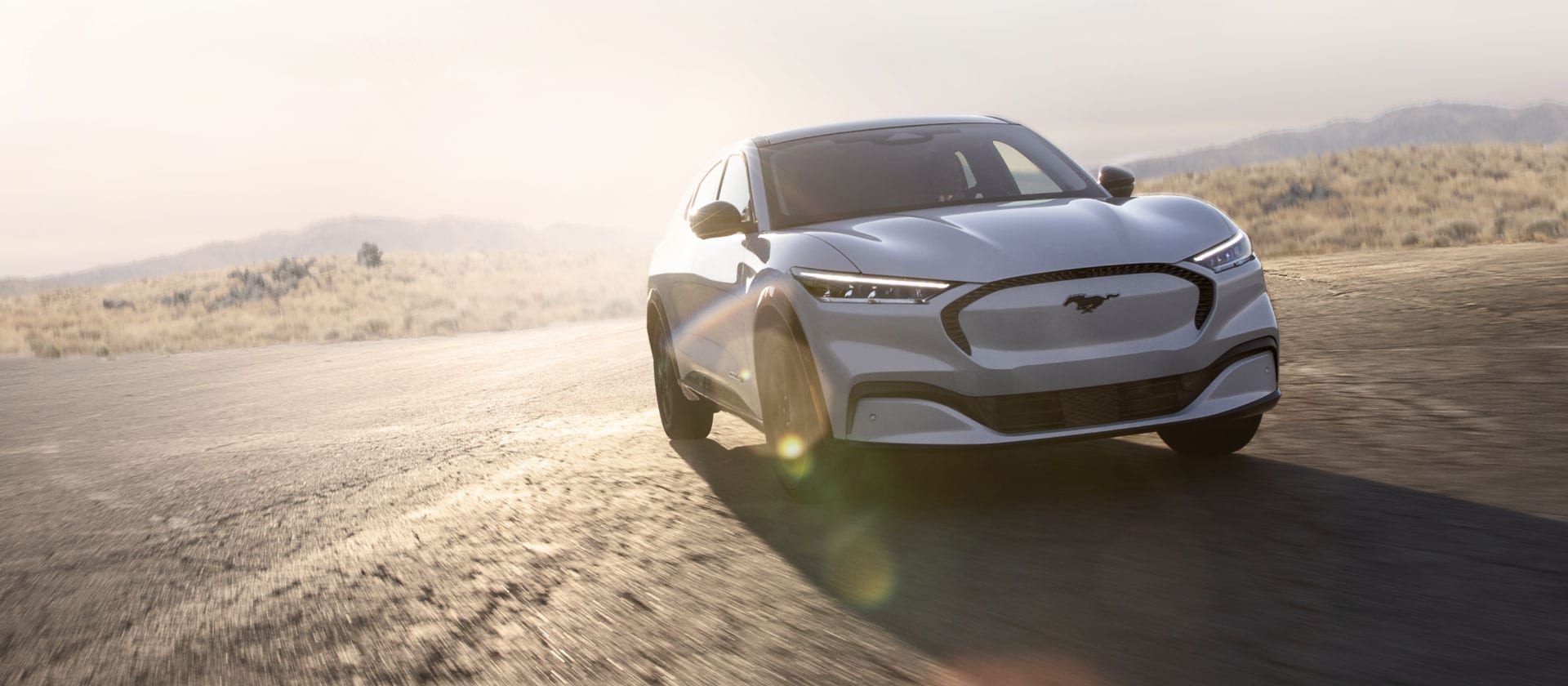 Stříbrný elektromobil Ford Mustang Mach-E jedoucí po dlouhé otevřené silnici.