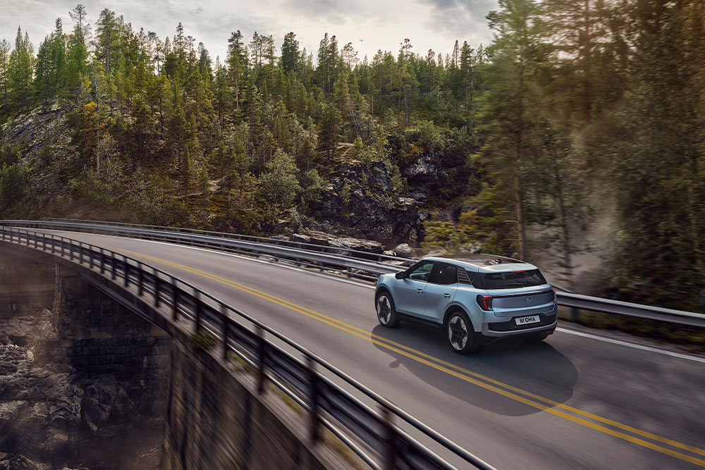 Modrý elektrický Ford Exlorer jedoucí po malebné venkovské silnici.