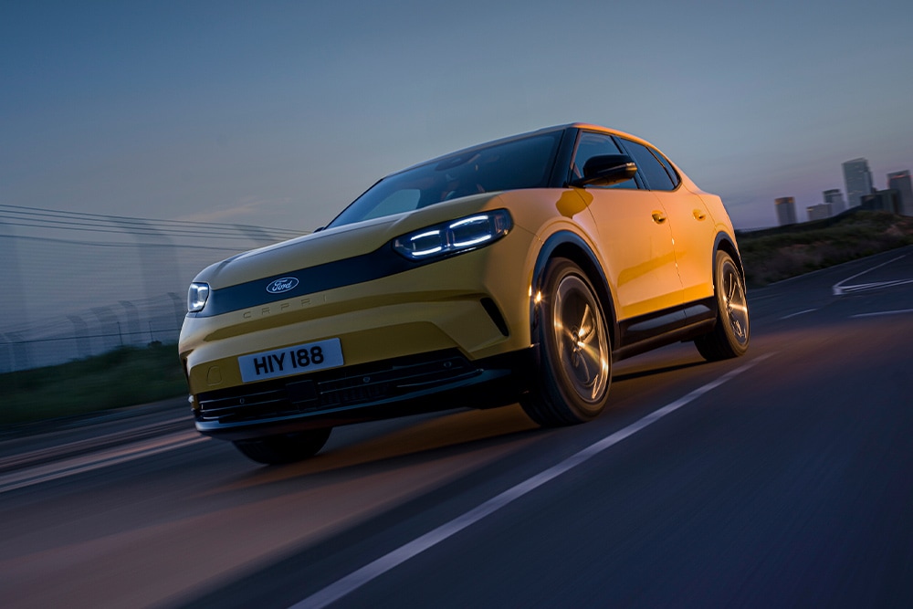 Žlutý elektromobil Ford Capri jedoucí po otevřené silnici.