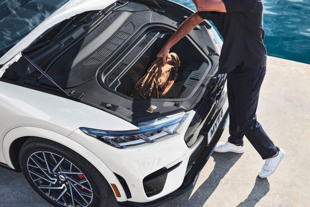 Osoba ukládající příruční tašku do zavazadlového prostoru bílého elektromobilu Ford Mustang Mach-E.
