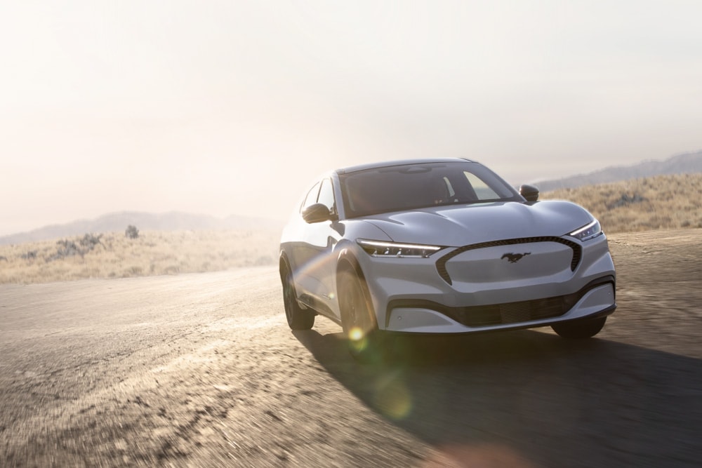 Stříbrný elektrický Ford Mustang Mach-E GT jedoucí po vyhlídkové silnici.