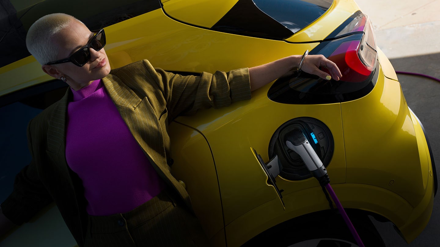 A woman leaning against a yellow electric Ford Capri that is connected to an EV charger.