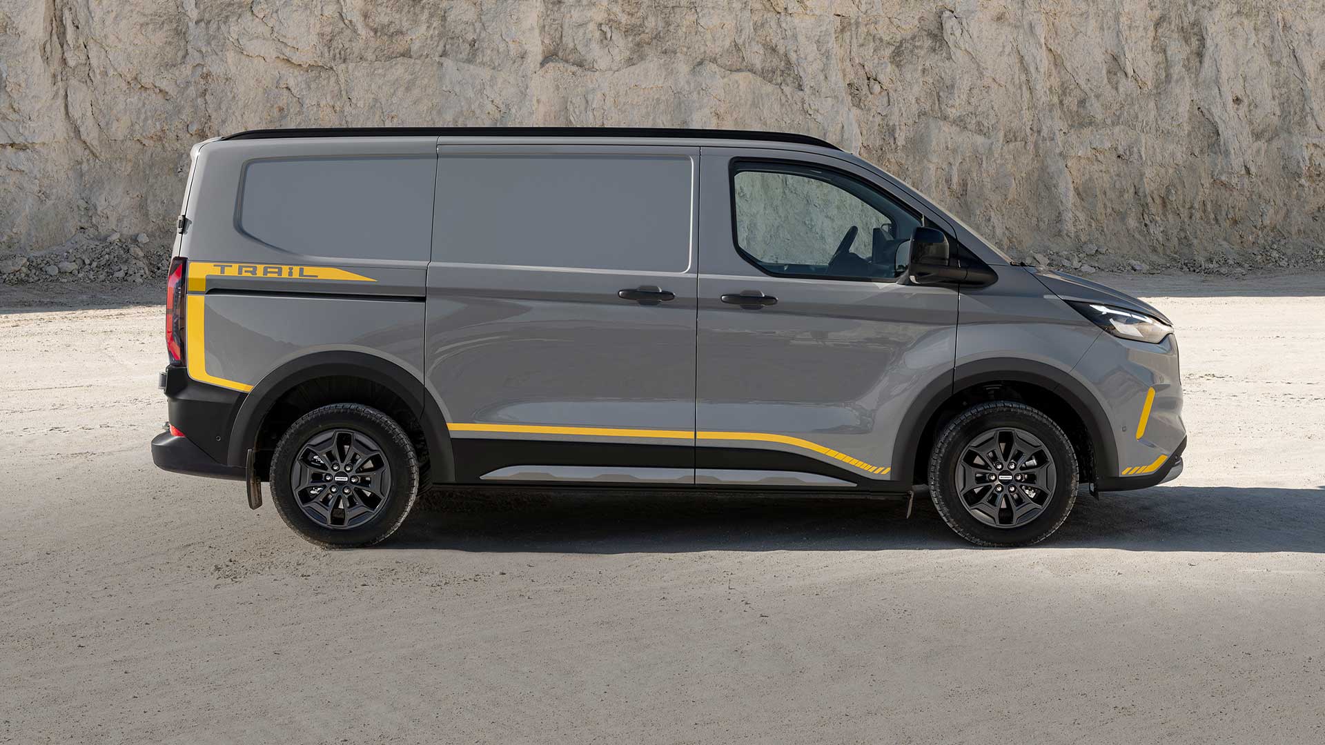 Boční pohled na šedou dodávku Ford Transit Custom Trail se žlutými polepy.