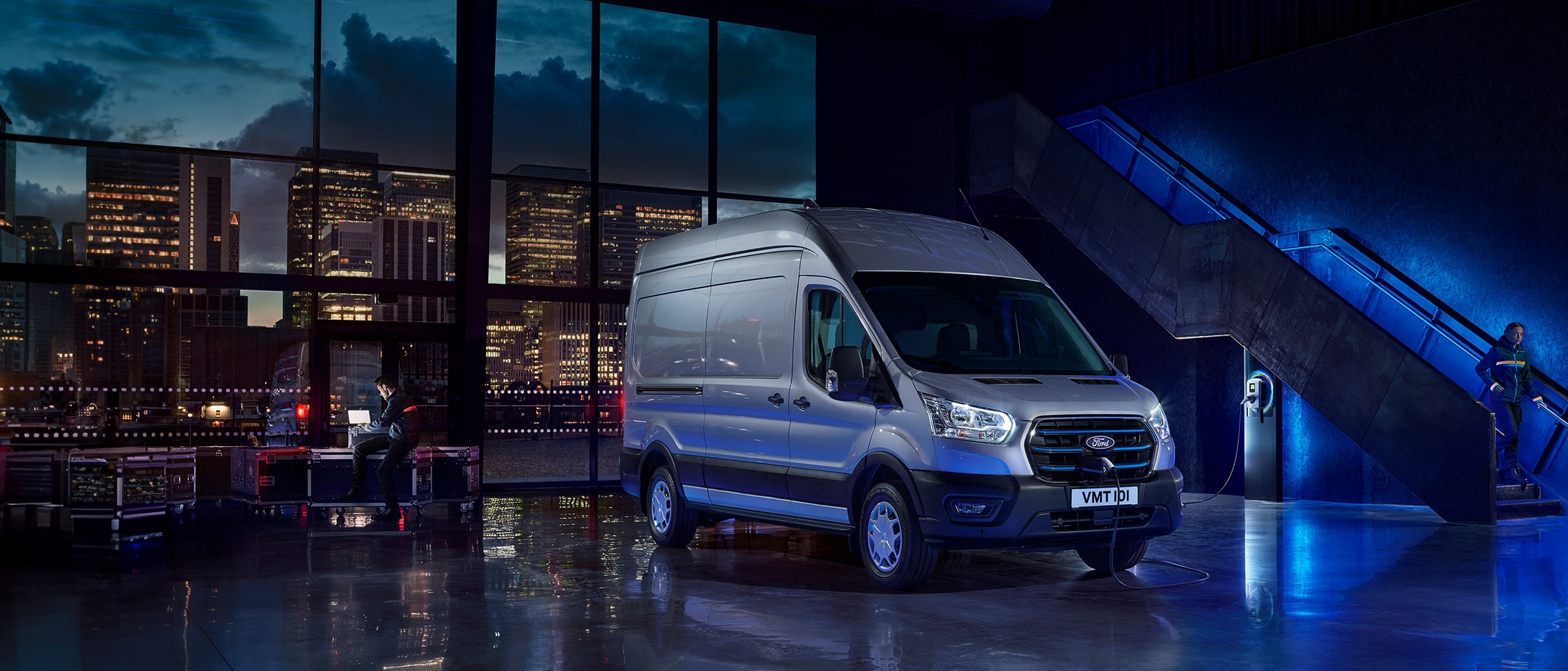 New E-Transit side view with the backdrop of city in night with blue electric lights New E-Transit side view with the backdrop of city in night with blue electric lights