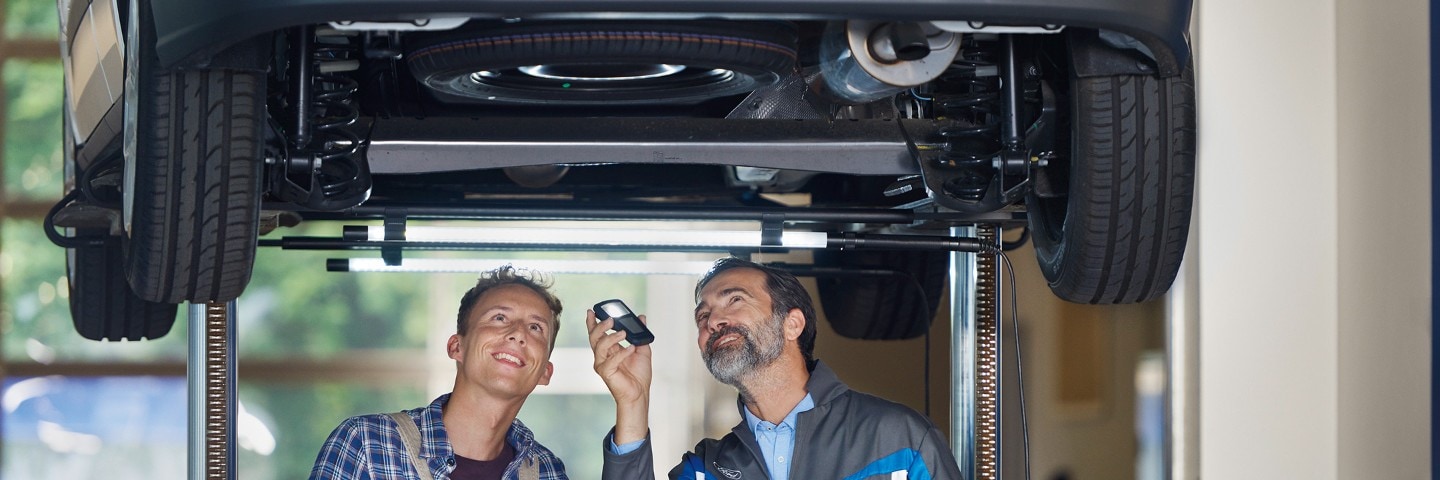 Service employee and customer standing under the car at workshop Service employee and customer standing under the car at workshop
